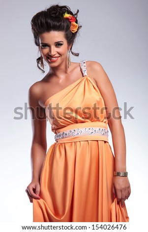 young fashion woman smiling for the camera while holding her dress with both hands. on gray background