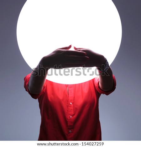 young casual woman covering her mouth over a shiny blank circle. speak no evil concept. on gray background