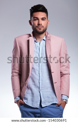 young casual man standing with his hands in his pockets and his lapels raised while looking into the camera. on gray background