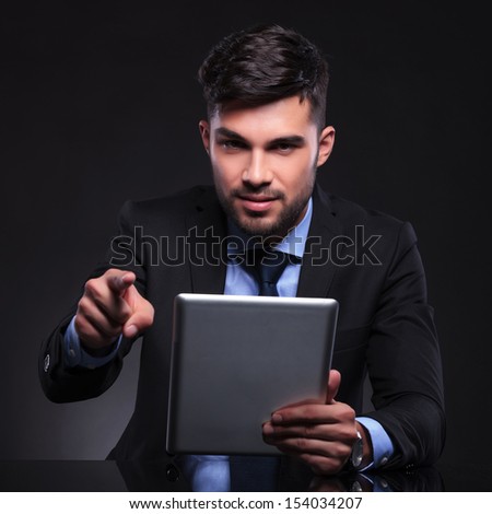 young business man holding his tablet and pointing at the camera. on black background