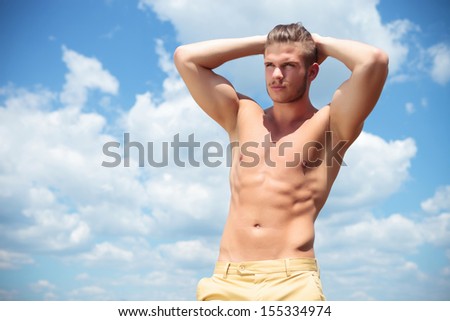 young topless man posing outdoor with his hands at the back of his head while looking away