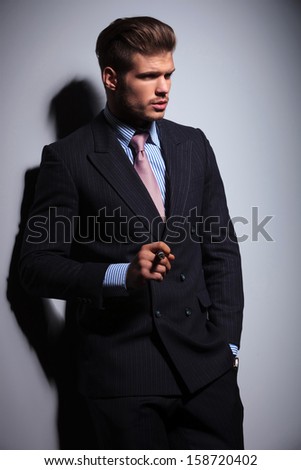 side view of a fashion man in suit and tie smoking a cigar on gray background