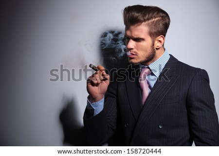 side view of a fashion model in suit and tie enjoying his cigar on gray background