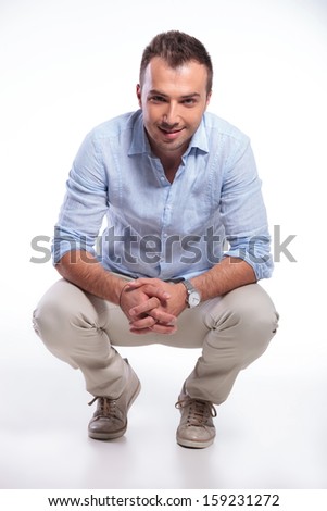 young casual man posing in a crouched position with his hands together and smiling for the camera. on gray background