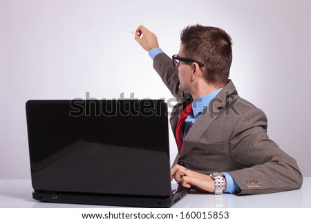 young business man sitting at laptop and writing on an imaginary screen behind him. on a gray background