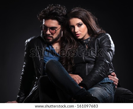 embraced seated couple in leather jackets pose on a dark studio background