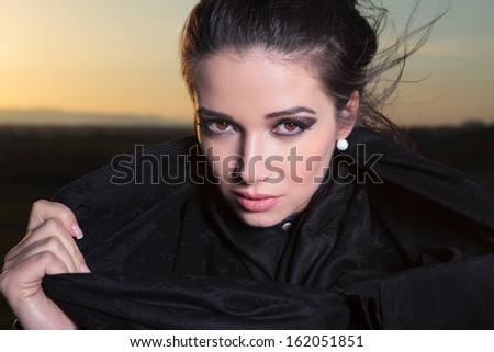 close up picture of a beautiful woman pulling her scarf and looking to the camera in the dusk of the day