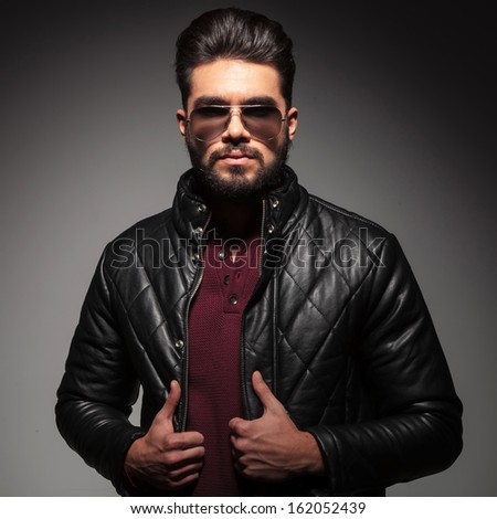 young man with a bad boy look , wearing leather jacket and sunglasses, on gray background