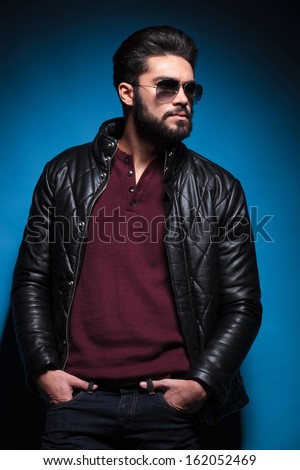 side view profile of a young bearded fashion man in leather jacket and sunglasses standing with his hands in pockets
