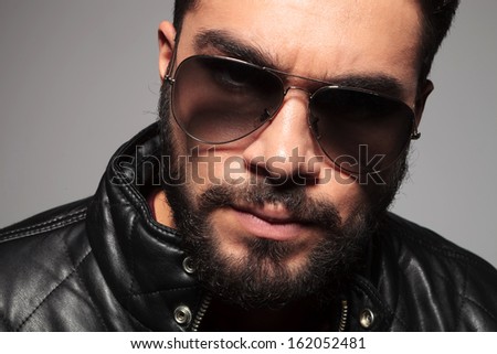 closeup picture of a young man with long beard wearing sunglasses and leather jacket looking at the camera