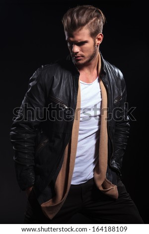 side view of a fashion man in leather jacket is looking to his back on dark background - stock photo