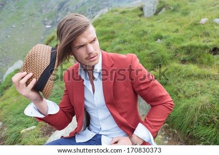 seated young man taking his hat off and looks away , outdoor picture