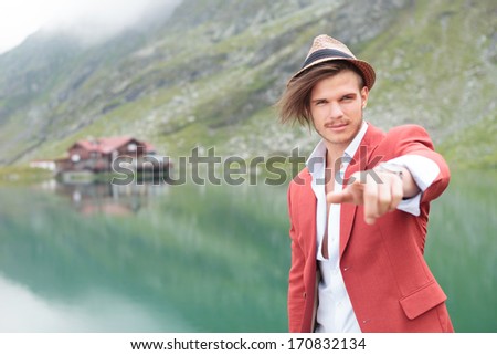 young man holding a trip bag walking in front of a mountain lake with cabin