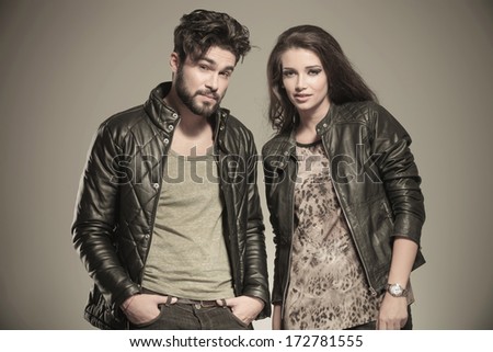 modern couple in leather clothes standing next to each other and looking at the camera in studio
