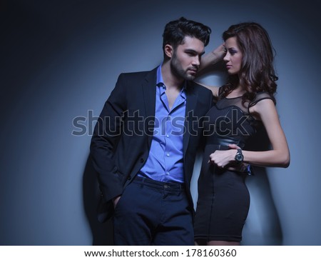 portrait of a young fashion man holding a beautiful woman while looking away with his hand in his pocket. on a dark blue background
