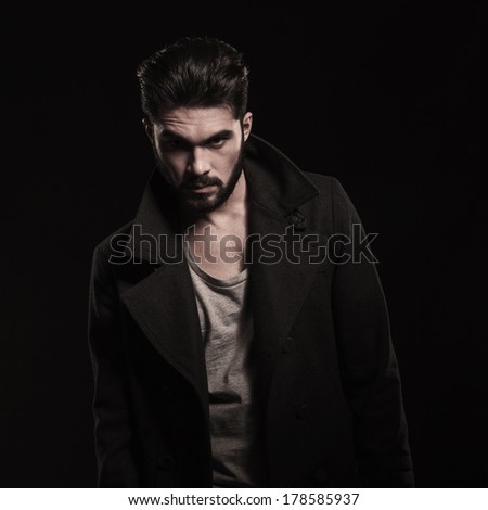 fashion young man with beard wearing long coat with big collars looking at the camera