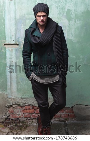 young fashion man posing in front of a cracked wall with his hands in his pocket and looking into the camera