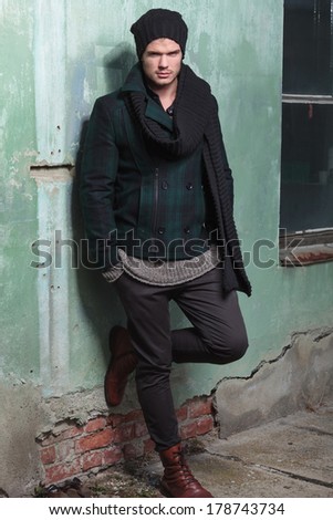 young fashion man posing with his foot on an old wall while holding his hands in his pockets and looking into the camera