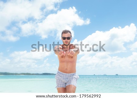 excited young man in bathing suit pointing to the camera while standing on the beach