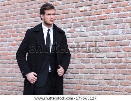 young business man walking by a brick wall and looking up, away from the camera