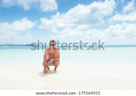 crouched man in swim suit and sunglasses on the beach of mauritius