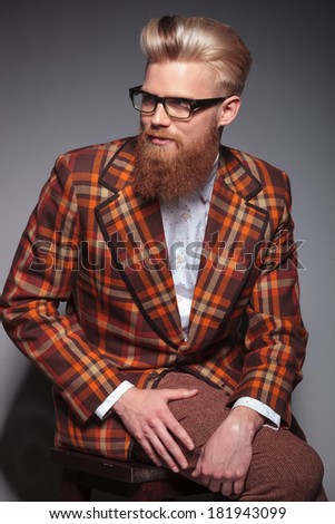 smiling fashion man with beard and nice hairstyle looking away from the camera while sitting