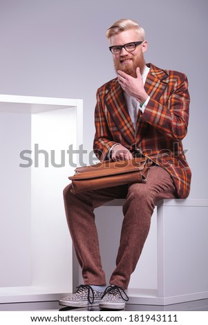 fashion young man is laughing while playing with his beard , sitting in studio