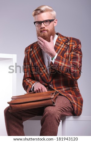 fashion man sitting and playing with his long beard in studio