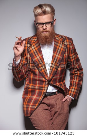 serious fashion man with beard and nice hairstyle smoking a cigarette and looks at the camera
