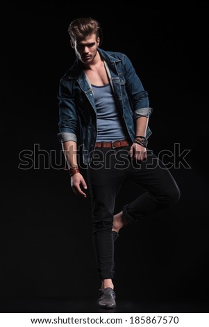 young fashion man in casual clothes standing on one leg in a fashion pose in studio