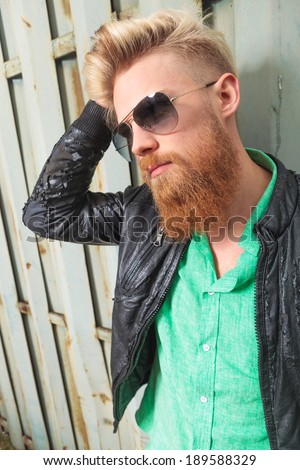 close up portrait of a young casual redhead bearded man with his hand in his hair, looking away from the camera