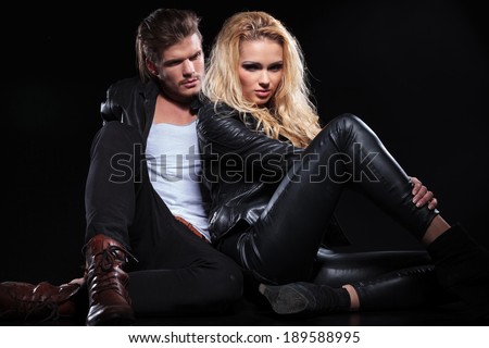 young beautiful woman leaning on her man and looking into the camera while he is looking at her . on black background