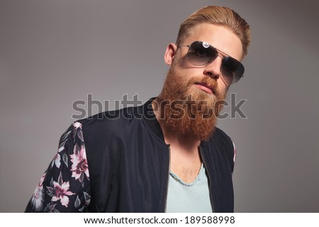 portrait of a casual young man with a long red beard looking into the camera. on gray studio background