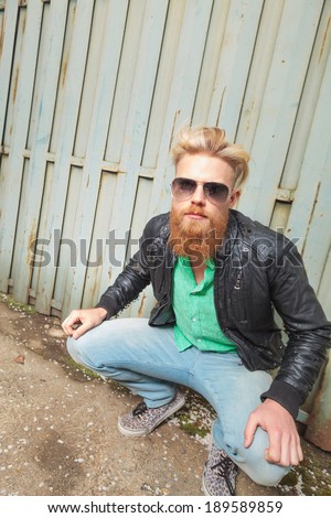 young casual redhead bearded man posing in a crouched position while looking into the camera with his hands on his knees