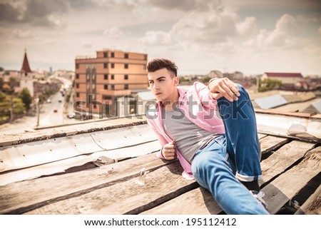 side view of a relaxed young man lying on the roof top of a building with city in the background