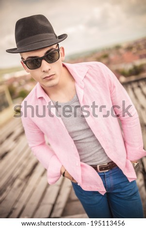 casual fashion young man with hat and sunglasses standing with hands in his pockets