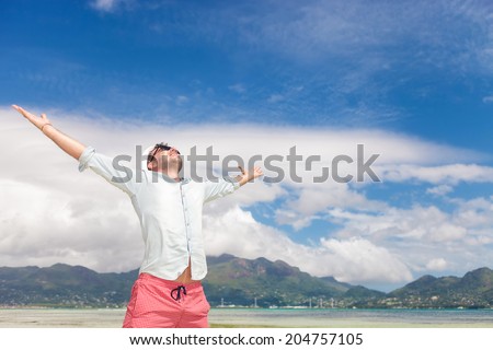 joy of life and freedom expressed by a young man on the beach, standing with hands in the air