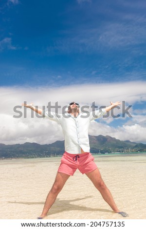 young casual man celebrating life with hands in the air on a perfect beach in the seychelles