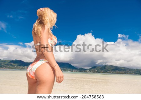 back of a sexy blonde woman on the beach looking away to beautiful view