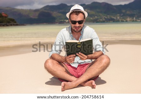 smiling young man reading a good book while sitting on the beach