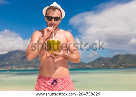 attractive man drinks coconut juice from a nut on a beach at the sea