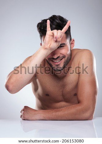 seated naked man making a rock and roll hand sign, studio picture
