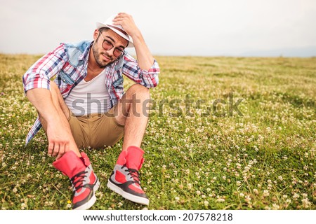 young man saying hello holding hat while sitting on a field