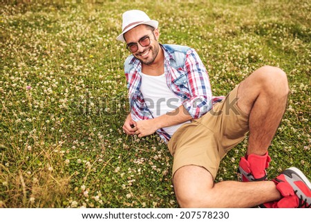 relaxed casual man with hat and glasses laying down on a field and smiles