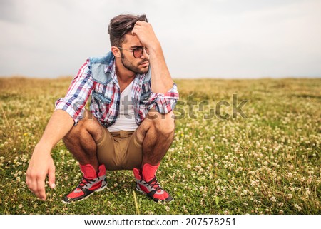 crouched casual man in a grass field thinking and looking away to his side