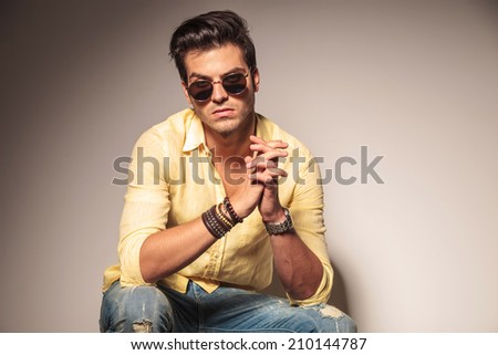 casual man with sunglasses seats on chair and looks to the camera