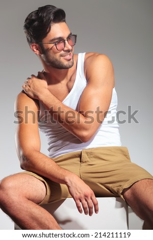 side view of a sexy seated man with hand on shoulder looking away to his side