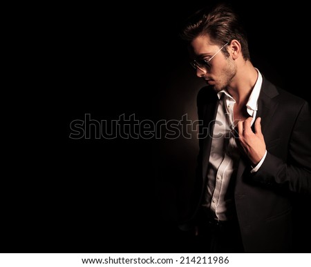 side view of a cool fashion man in suit and sunglasses pulling his collar and looking down