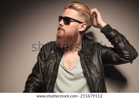 Casual young man in leather jacket pulling his sunglasses, sitting on the floor, looking at the camera