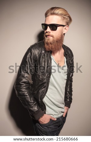 Fashion man in leather jacket looking down, sitting and holding his hands, studio shot